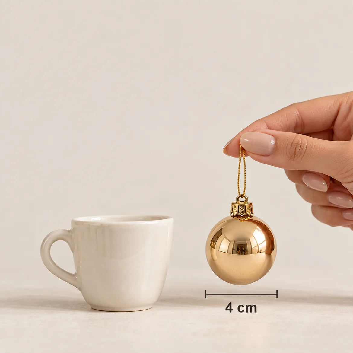 Mão segurando uma bola Merano de 4 cm pelo cordão, ao lado de uma xícara de café
