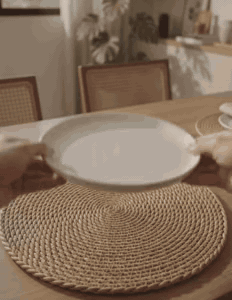 Prato sendo colocado sobre o jogo americano Toscana, detalhe do trançado e a mesa pronta